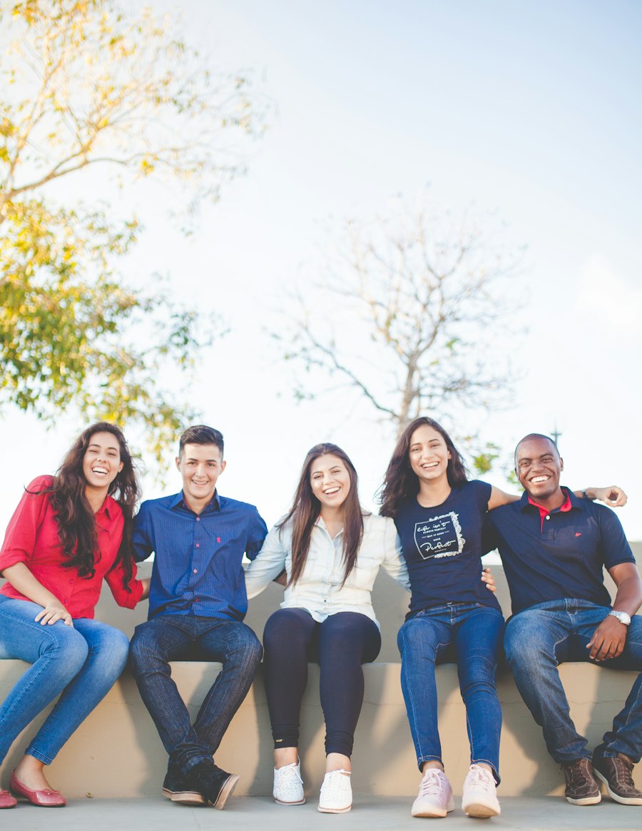Five friends sitting close together outdoors and smiling